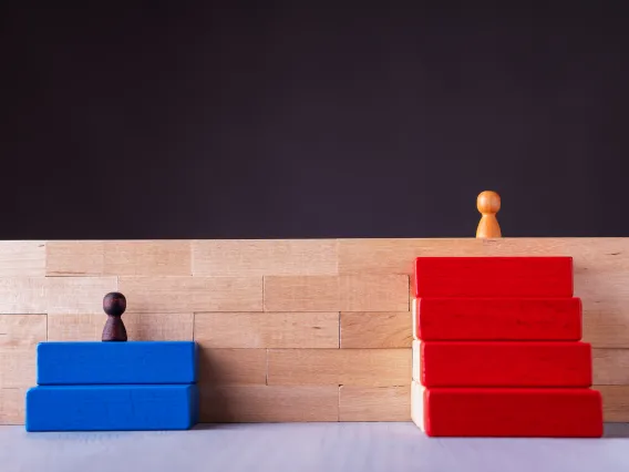 Wooden blocks, wooden people, one above, one below signaling inequality