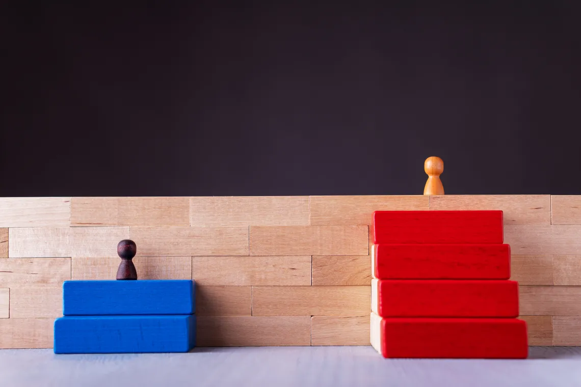 Wooden blocks, wooden people, one above, one below signaling inequality